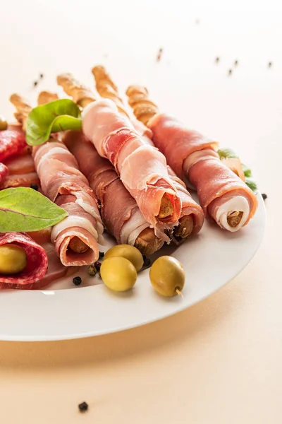 Delicious meat platter served with olives and breadsticks on plate on beige background — Stock Photo