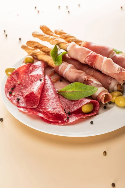Köstliche Fleischplatte serviert mit Oliven und Semmelstangen auf Teller auf beigem Hintergrund — Stockfoto