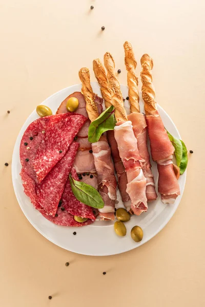 Vista superior de deliciosa bandeja de carne servida con aceitunas y palitos de pan en el plato sobre fondo beige - foto de stock