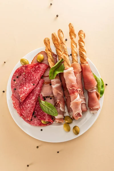 Вид на вкусное мясное блюдо подается с оливками и хлебными палочками на тарелке на бежевом фоне — стоковое фото