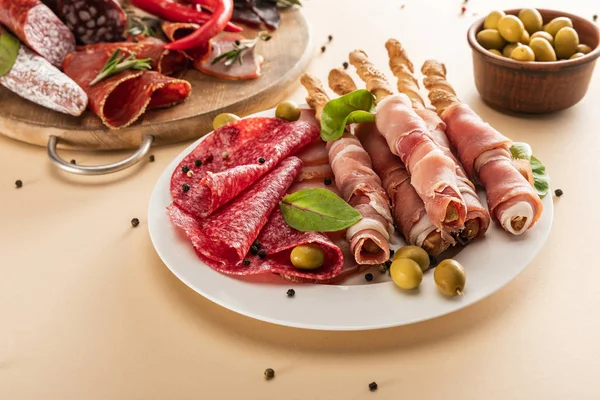 Delicious meat platters served with olives, spices and breadsticks on plate and wooden board on beige background — Stock Photo