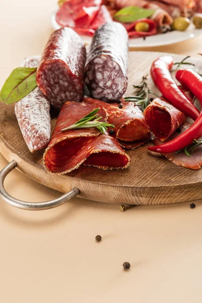 Delicious meat platters served with rosemary and chili pepper on wooden board on beige background — Stock Photo