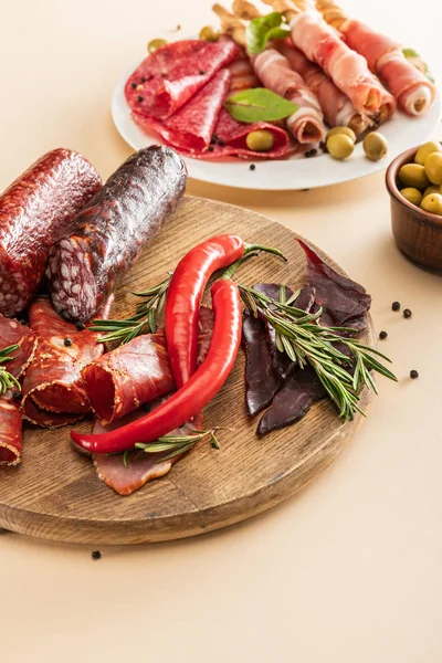 Deliciosos pratos de carne servidos com azeitonas, especiarias e breadsticks na placa e placa de madeira no fundo bege — Fotografia de Stock