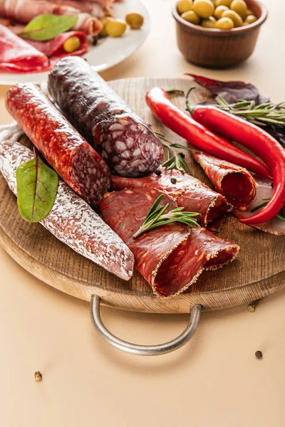 Deliciosos pratos de carne servidos com alecrim e pimenta em tábua de madeira em fundo bege — Fotografia de Stock