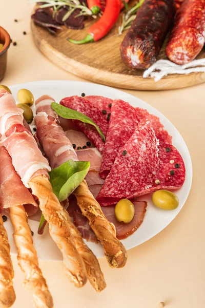 Délicieux plats de viande servis avec des olives, des épices et des bâtonnets de pain sur plaque et planche de bois sur fond beige — Photo de stock