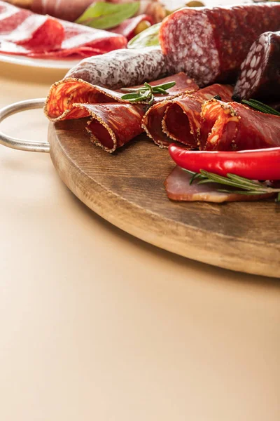 Deliciosos pratos de carne servidos com alecrim e pimenta em tábua de madeira em fundo bege — Fotografia de Stock