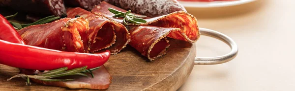 Delicious meat platters served with rosemary and chili pepper on wooden board on beige background, panoramic shot — Stock Photo