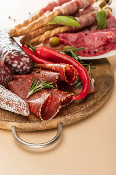 Deliziosi piatti di carne serviti con olive, spezie e grissini su piatto e tavola di legno su sfondo beige — Foto stock