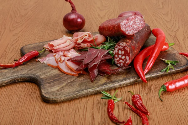 Delicious meat platter served with chili pepper and rosemary on wooden table — Stock Photo