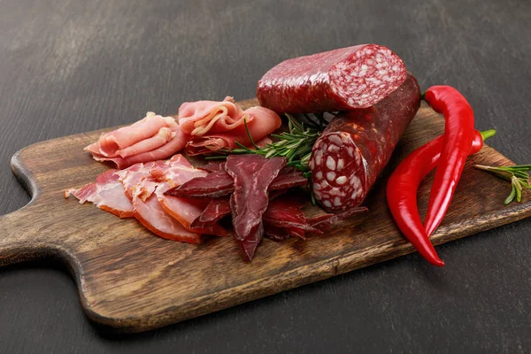 Délicieux plateau de viande servi avec du piment et du romarin sur une table noire en bois — Photo de stock