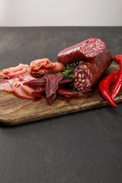 Délicieux plateau de viande servi avec du piment et du romarin sur une table noire en bois — Photo de stock