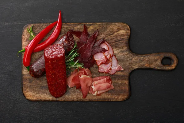 Vista superior de deliciosa bandeja de carne servida com pimenta e alecrim em mesa preta de madeira — Fotografia de Stock