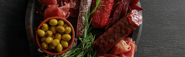 Vista dall'alto di delizioso piatto di carne servito con olive ed erbe aromatiche su tavolo nero in legno, colpo panoramico — Foto stock