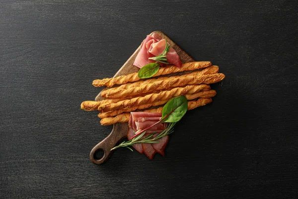 Верхний вид вкусного мясного блюда подается с хлебными палочками и травами на борту на деревянный черный стол — стоковое фото