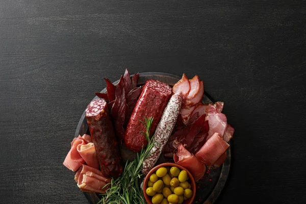 Vue du dessus de délicieux plateau de viande servi avec des olives et des herbes sur une table noire en bois — Photo de stock