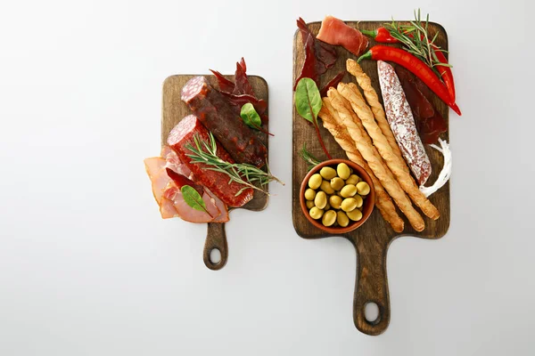 Vista dall'alto di deliziosi piatti di carne serviti con grissini, olive, peperoncini ed erbe aromatiche su tavole isolate su bianco — Foto stock