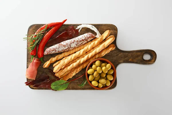 Top view of delicious meat platter served with breadsticks, olives, chili peppers and herbs on board isolated on white — Stock Photo