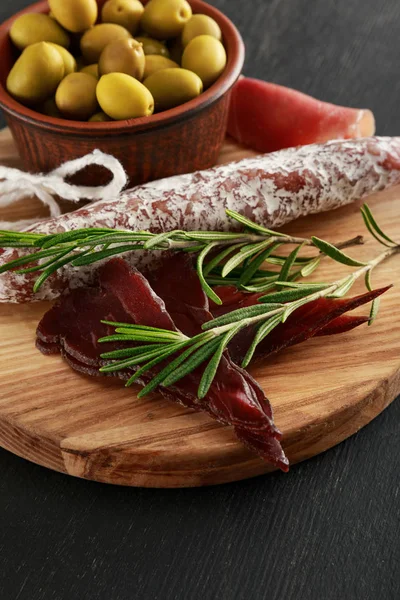 Вкусное мясное блюдо подается с оливками на борту на черной поверхности — стоковое фото