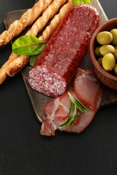 Délicieux plateau de viande servi avec des olives et des grissini à bord sur une surface noire — Photo de stock