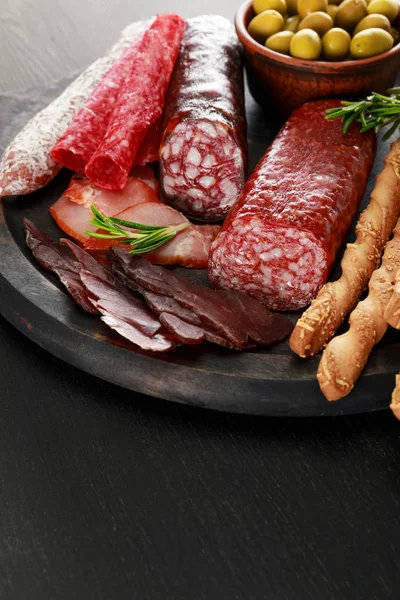 Вкусное мясное блюдо подается с оливками и гриссини на борту на черной поверхности — стоковое фото