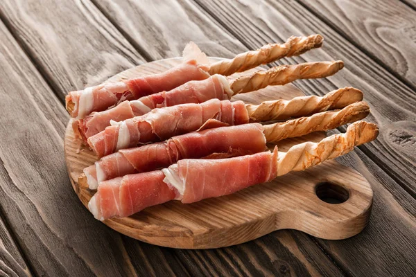 Deliciosa bandeja de carne con grissini y jamón sobre tabla de madera - foto de stock