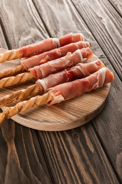 Délicieux plateau de viande avec grissini et prosciutto sur planche de bois — Photo de stock