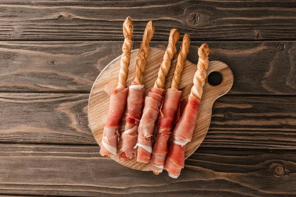 Vista superior de deliciosa bandeja de carne con palitos de pan y jamón sobre tabla de madera - foto de stock