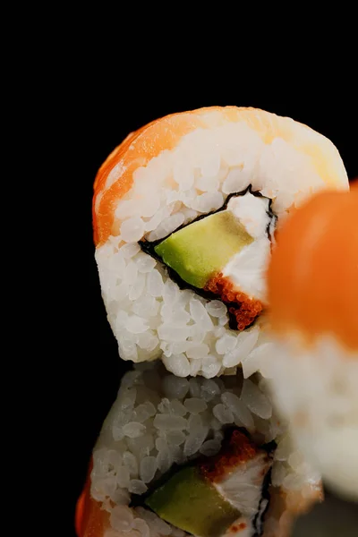 Selective focus of fresh delicious Philadelphia sushi piece with avocado, creamy cheese, salmon and masago caviar isolated on black — Stock Photo