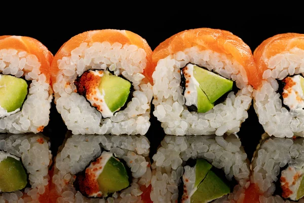 Fresco delicioso sushi Filadelfia con aguacate, queso cremoso, salmón y caviar masago aislado en negro con reflejo - foto de stock