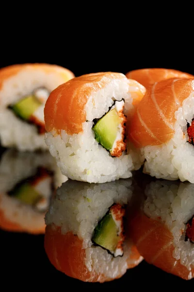 Close up view of fresh delicious Philadelphia sushi with avocado, creamy cheese, salmon and masago caviar isolated on black with reflection — Stock Photo