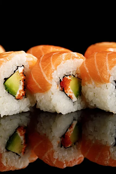 Vista de cerca del delicioso sushi fresco de Filadelfia con aguacate, queso cremoso, salmón y caviar masago aislado en negro con reflejo - foto de stock