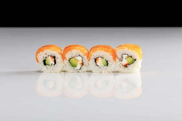 Delicious Philadelphia sushi with avocado, creamy cheese, salmon and masago caviar on white surface isolated on black — Stock Photo