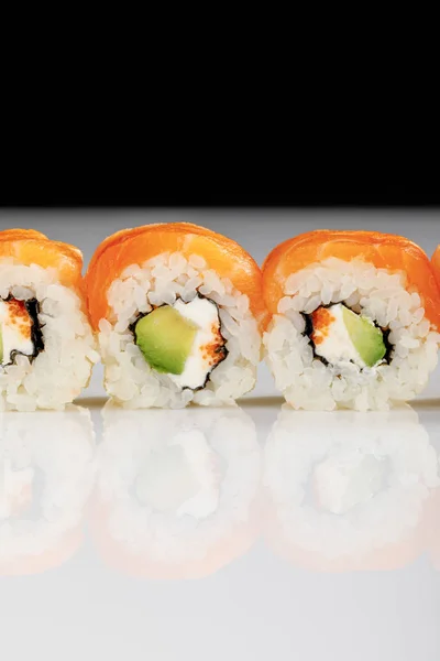 Close up view of delicious Philadelphia sushi with avocado, creamy cheese, salmon and masago caviar on white surface isolated on black — Stock Photo