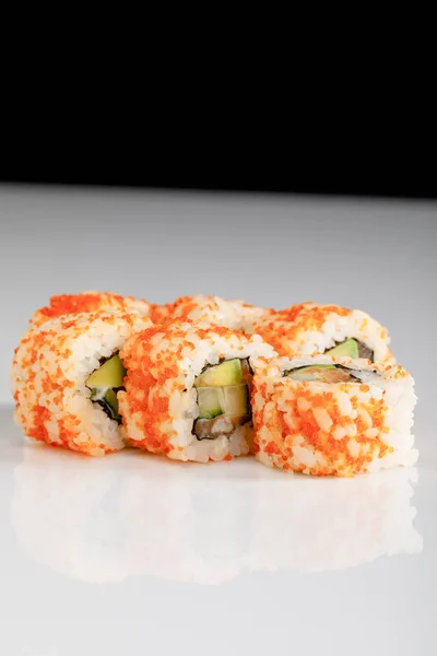 Delicious California roll with avocado, salmon and masago caviar on white surface isolated on black — Stock Photo