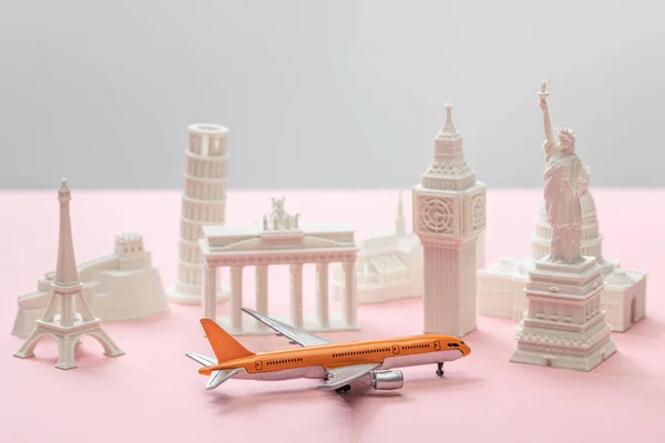 Spielzeugflugzeug in der Nähe von kleinen Statuetten verschiedener Länder auf grau und rosa — Stockfoto