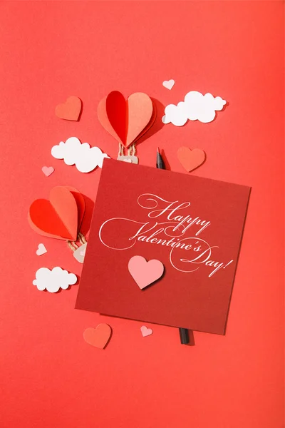 Top view of paper heart shaped air balloons in clouds near card with happy valentines day lettering on red background — Stock Photo