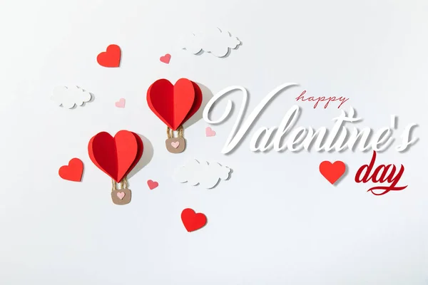 Top view of paper heart shaped air balloons in clouds near happy valentines day lettering on white background — Stock Photo