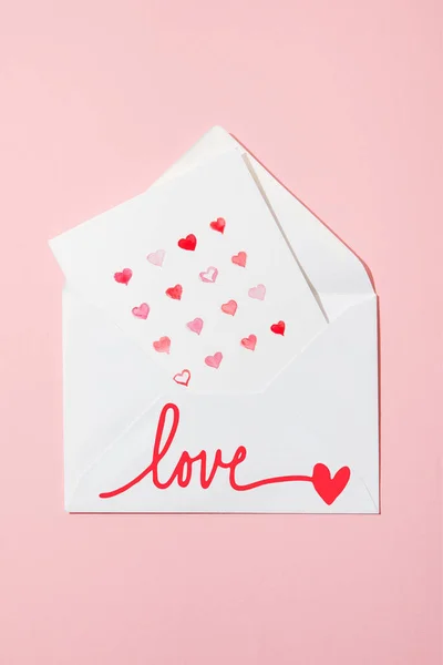 Top view of greeting card with hearts in white envelope with love lettering on pink — Stock Photo