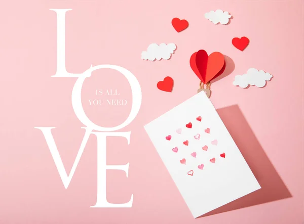 Vista dall'alto del biglietto di auguri con cuori vicino alla carta palloncino d'aria a forma di cuore nelle nuvole e l'amore è tutto ciò che serve lettering su rosa — Foto stock