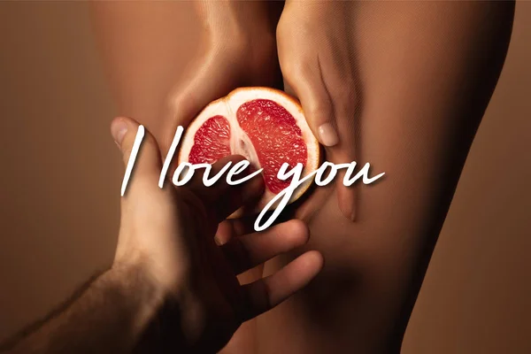 Cropped view of man reaching woman in nylon tights holding grapefruit half near i love you lettering on brown — Stock Photo