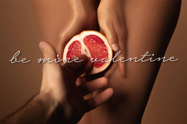 Cropped view of man reaching woman in nylon tights holding grapefruit half near be mine valentine lettering on brown — Stock Photo