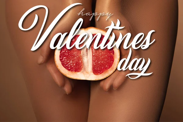 Cropped view of woman in nylon tights holding grapefruit half near happy valentines day lettering on brown — Stock Photo