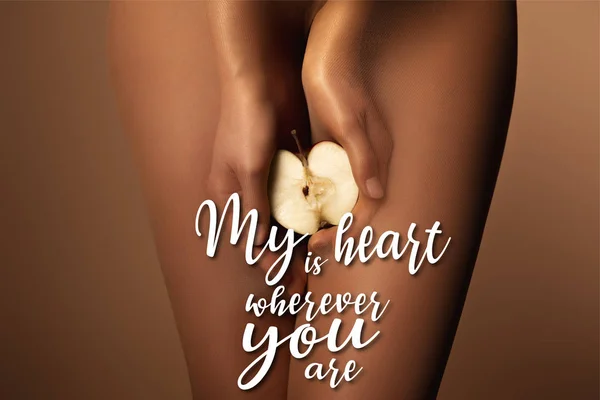 Cropped view of woman in nylon tights holding apple half near my heart is wherever you are lettering on brown — Stock Photo