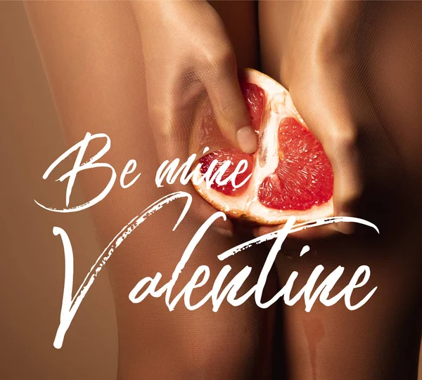 Cropped view of woman in nylon tights holding grapefruit half near be mine valentine lettering on brown — Stock Photo