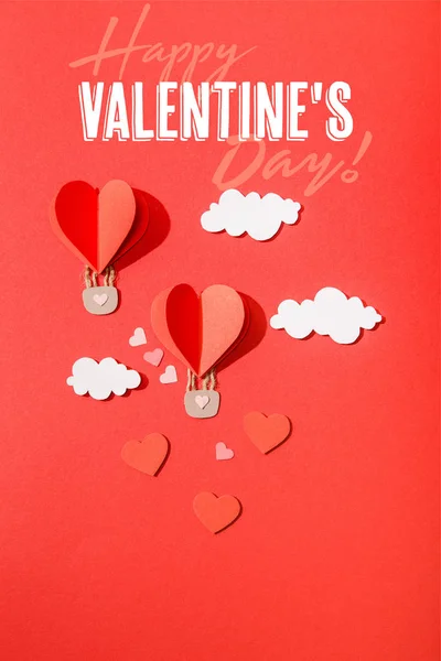 Top view of paper heart shaped air balloons in clouds near happy valentines day lettering on red background — Stock Photo