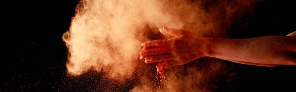 Mãos femininas perto de laranja colorido holi pintura explosão no fundo preto, tiro panorâmico — Fotografia de Stock