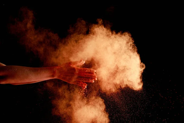 Weibliche Hände in der Nähe orangefarbener Holi-Farbe Explosion auf schwarzem Hintergrund — Stockfoto