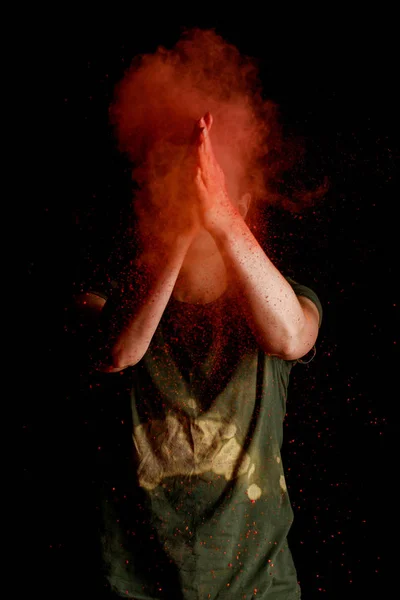 Woman with orange colorful holi paint explosion in front of face on black background — Stock Photo