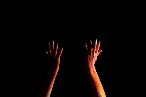 Vue recadrée des mains féminines avec de la poudre de peinture holi colorée orange isolée sur noir — Photo de stock