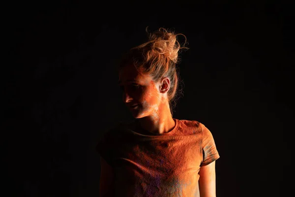 Woman with orange colorful holi paint powder on skin and clothes isolated on black — Stock Photo